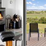 Indoor space with fireplace and outdoor terrace with seating and view of field and wind turbines.