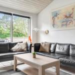 Zwei schwarze Ledersofas stehen um einen Holztisch herum. Große Fenster zeigen einen grünen Außenbereich.