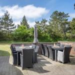 Terrasse mit zwei Tischen, Stühlen und einem geschlossenen Sonnenschirm. Hintergrund: Bäume und Himmel.