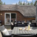 Terrasse mit Tisch, Stühlen und Sonnenschirm vor einem Haus mit Strohdach und Backsteinwand.