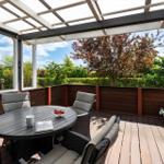 Terrasse mit Sitzgruppe, Tisch und Pflanzen. Glasdach und Holzgeländer.