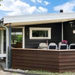 Haus mit Terrasse, Sitzgruppe und Blumen. Helle Fenster und dunkle Fassade.