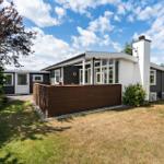 Moderne Villa mit Terrasse, Garten und weißem Schornstein unter blauem Himmel.