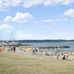 Strand mit Booten, Leuten und Rettungswache unter blauem Himmel.