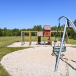 Kinderspielplatz mit Sandkasten, Klettergerüst und Schaukel auf grünem Rasen.