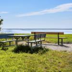 Picknicktisch und Bänke am Ufer mit Blick auf Wasser und Gras.