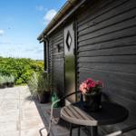 Terrace with table, chairs, and plants in front of a wooden house.