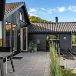 Black wooden house with terrace, sun loungers, and garden. Large windows and roof overhang.