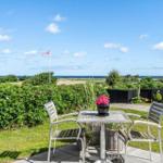 Terrace with table and chairs, view of green areas and sea under blue sky.