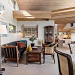 Living and dining area with wooden ceiling, sofa, table, and chairs. Kitchen visible in background.