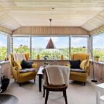 A room with two yellow armchairs, a stove, and large windows overlooking greenery.