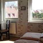 Schlafzimmer mit Bett, Schreibtisch und Fenstern zum Blick auf Dächer und Turm.