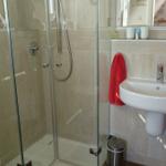 Badezimmer mit Dusche, Waschbecken und Toilette. Rote Handtücher und Spiegel sichtbar.