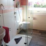 Badezimmer mit Dusche, Waschbecken und Toilette. Rote Handtücher und Fenster mit Blick.