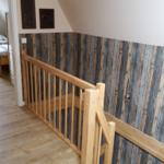 Holzgeländer und rustikale Wandverkleidung im Flur mit Blick in Schlafzimmer.
