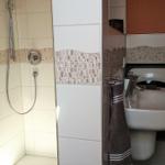Badezimmer mit Dusche, Waschbecken und Toilette. Fliesen mit Mosaikverzierung.