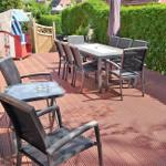 Terrasse mit Tisch, Stühlen und Liegestuhl. Holzdecke und grüne Hecke im Hintergrund.