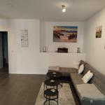 Wohnzimmer mit grauem Sofa, drei runden Tischen und Wandbildern.