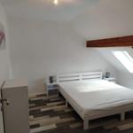Schlafzimmer mit Dachschrägen, weißem Bett und Holzboden. Dachfenster und Holzbalken sichtbar.