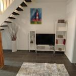 Wohnzimmer mit Fernseher, Regal und Treppe. Wandbild zeigt Leuchtturm.