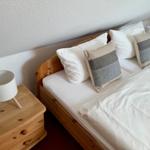 Ein Bett mit weißen Laken und Kissen, daneben ein Nachttisch mit Lampe.