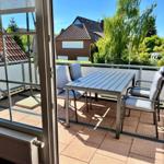 Terrasse mit Tisch und Stühlen, Blick auf Grün und Dächer.