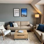 Wohnzimmer mit Sofa, Sessel, Couchtisch und Wandbildern.