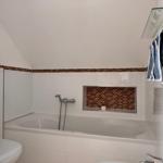 Badezimmer mit Badewanne, Duschwand und Mosaikfliesen an der Wand.