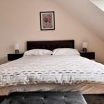 Schlafzimmer mit Doppelbett, Nachttischen und Wandbild unter Dachschrägen.