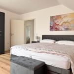 Schlafzimmer mit Doppelbett, Kleiderschrank und Wandbild mit Blumenmotiv.