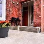 Roter Backsteinbau mit Terrasse, Grill und Pflanze. Eingang und Treppe sichtbar.