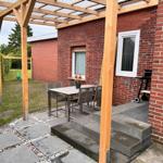 Terrasse mit Tisch, Stühlen und Grill neben rotem Backsteinhaus.