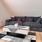 Ein Wohnzimmer mit grauem Sofa, weißem Couchtisch und Holzboden.