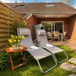 Zwei Liegestühle mit Handtuch und Tulpen auf grünem Rasen vor einer Terrasse.