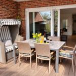 Terrasse mit Esstisch, Stühlen und Strandkorb. Durchgang ins Haus. Holzdecke und Backsteinwand.