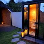 Außenliegende Sauna mit Holzwand und Glasfront. Beleuchtet durch Laterne und Innenbeleuchtung.