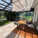 Terrasse mit Tisch und Stühlen unter Schutzdach und Sonnensegel.