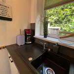 Küchenbereich mit Spüle, Kaffeemaschine und Fenster mit Blick auf Grün.