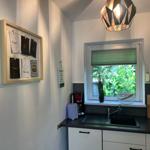 Küche mit Fenster, Spüle und Küchenzeile. Wand mit Bilderrahmen und Hängeschrank.