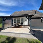 Haus mit Terrasse, Garten und Sitzgruppe unter Sonnenschutz.