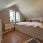 Schlafzimmer mit Dachschrägen, weißem Bett und zwei Fenstern mit Jalousien.
