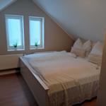 Schlafzimmer mit Dachschrägen, zwei Fenstern und Bett mit weißen Kissen.