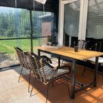 Terrasse mit Tisch und vier Stühlen, Blick auf grünen Garten.