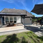 Haus mit Terrasse, Sitzgelegenheiten und Sonnenschutz. Grünflächen und gepflasterter Bereich.
