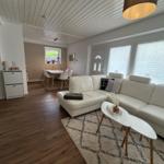 Wohnzimmer mit weißem Sofa, Holzboden und Fenstern mit Jalousien.