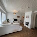 Wohnzimmer mit weißem Sofa, Holzboden und Kamin. Fenster mit Jalousien.