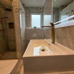 Bad mit Dusche, Waschbecken und Spiegel. Marmorwand und goldfarbene Armaturen.