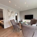 Wohnzimmer mit Sitzgelegenheiten, Fernseher und Blick in Schlafzimmer.