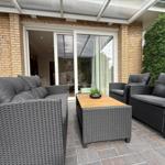 Terrasse mit grauem Rattan-Sofa, zwei Sesseln und Tisch unter Glasdach.
