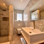 Badezimmer mit Dusche, Waschbecken und Toilette. Marmorwand und goldfarbene Details.